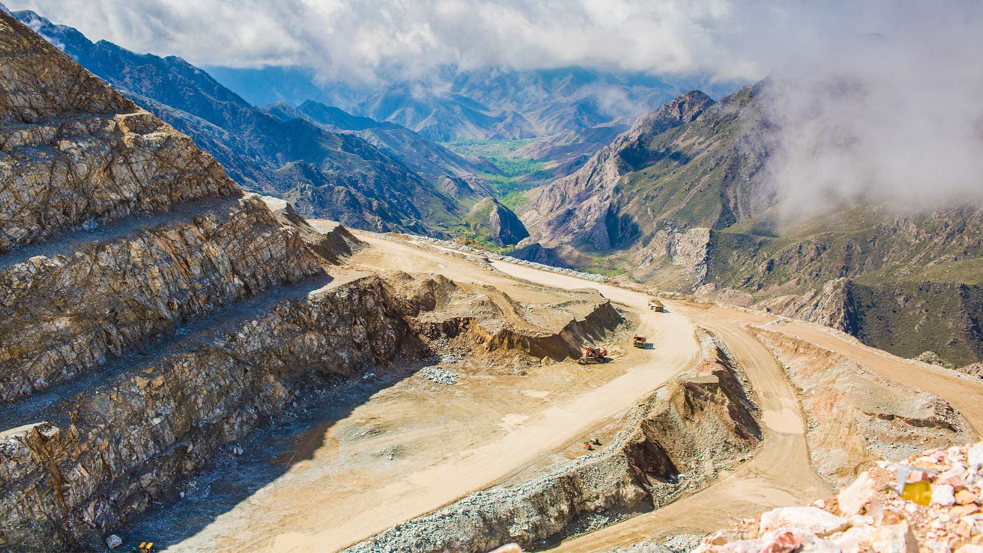 Elevated view of a Bozymchak road leading into a valley full of mountainous landscapes with low hanging clouds. 