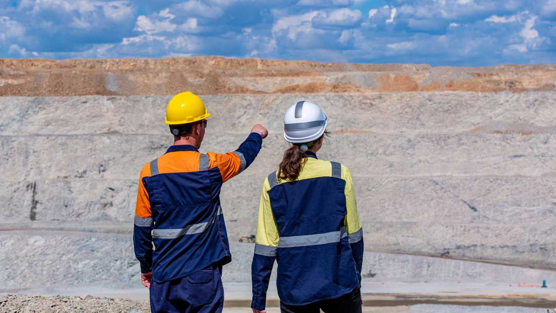 Two workers seen from behind pointing and staring into mountainous distance. 