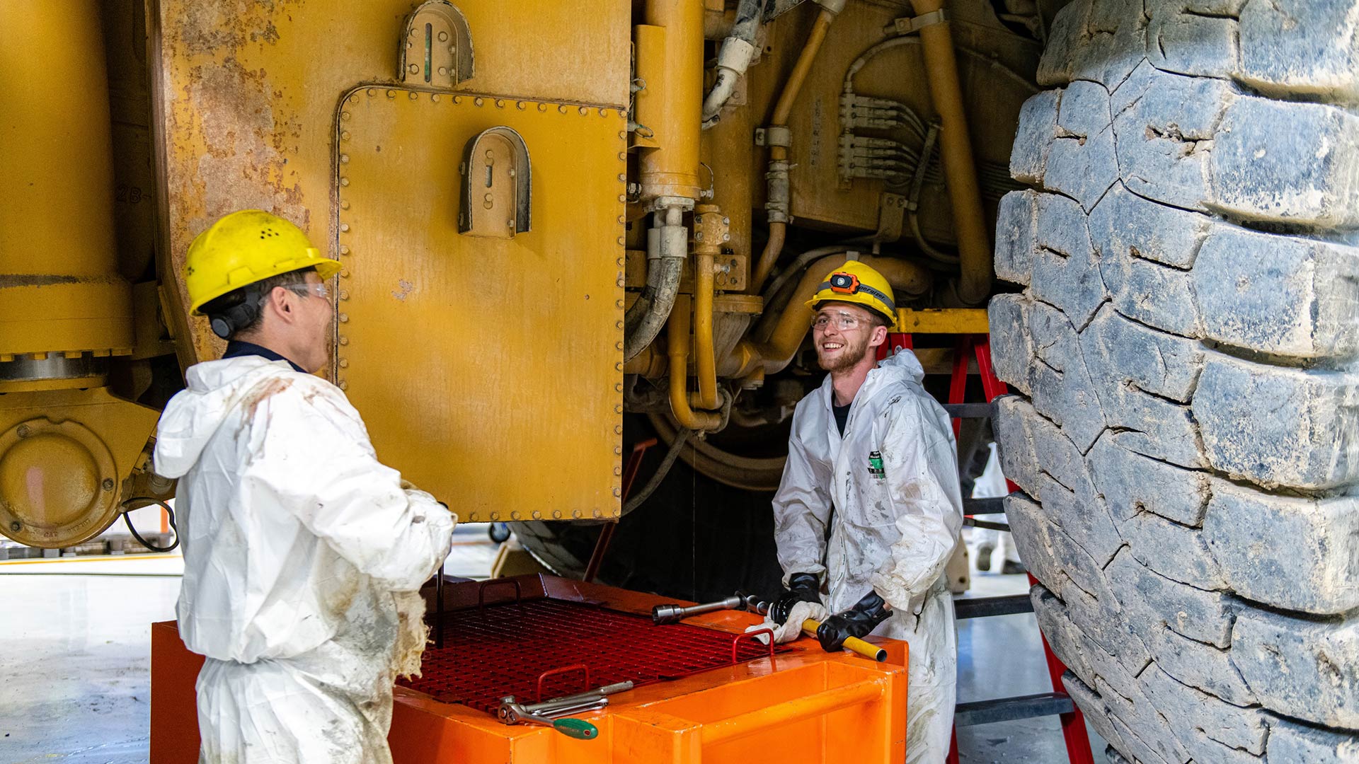 Two workers in safety gear working near a large vehicle. 