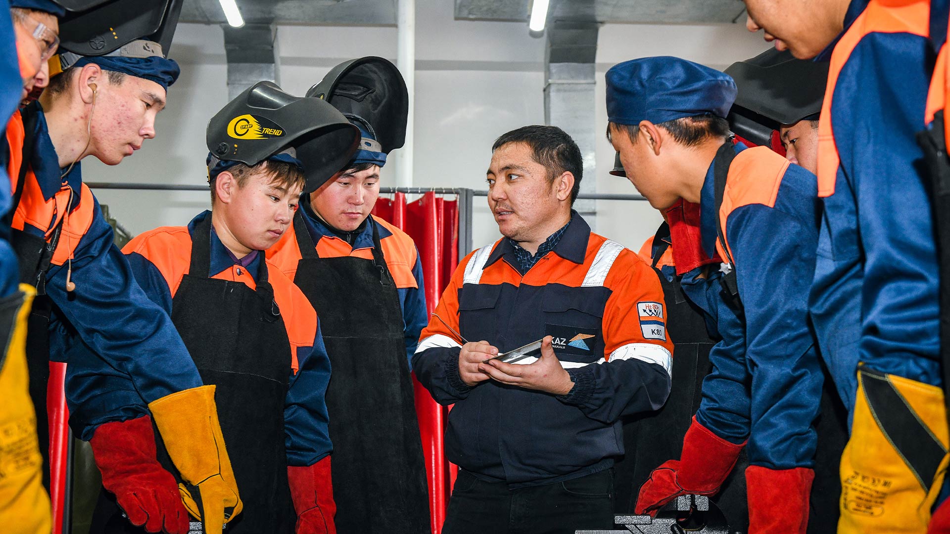 Көптеген жұмысшылар жиналып, пікірталас болды. Олар қорғаныс киімдері мен бас киімдер киеді.