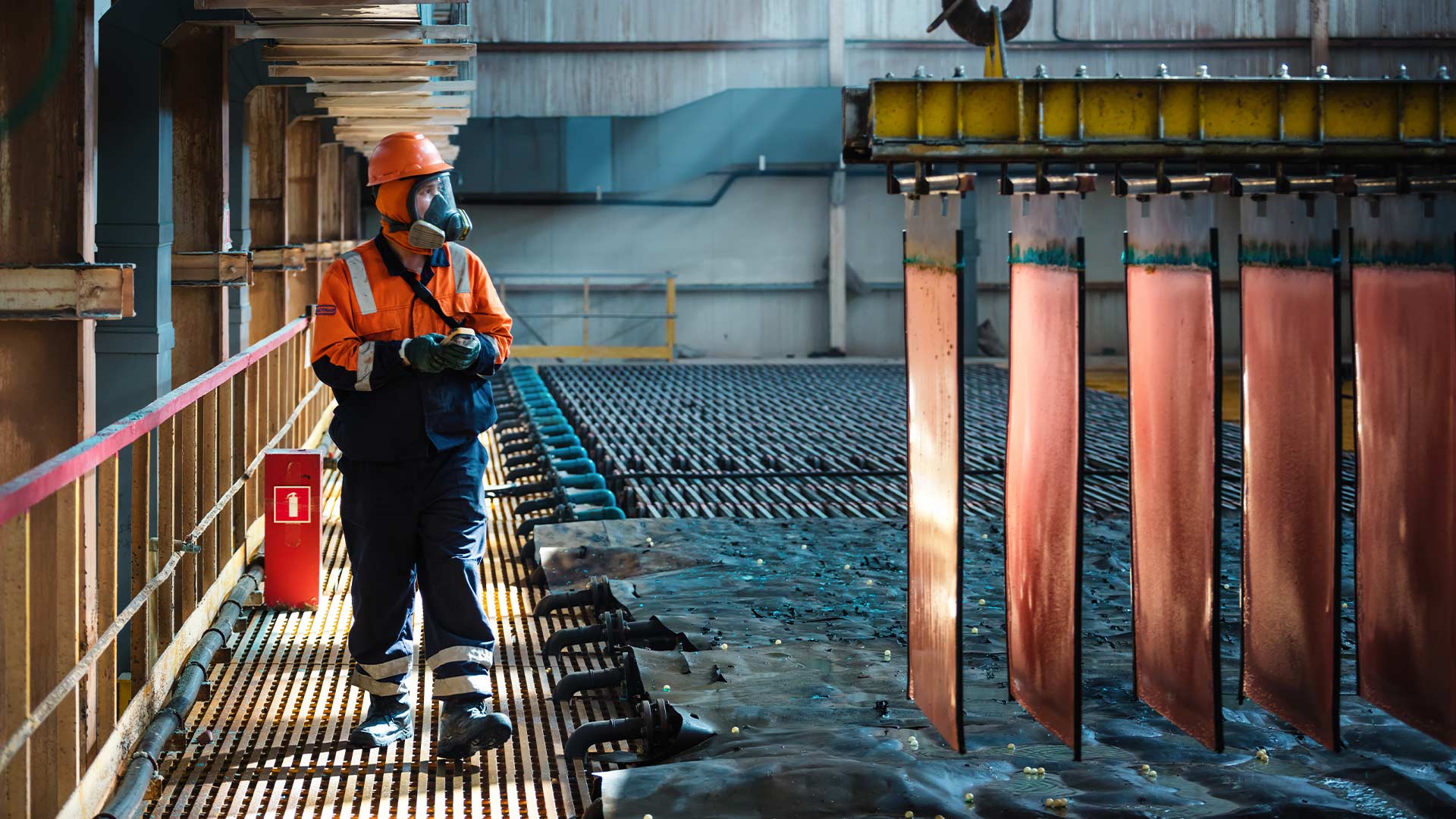 Worker standing on the sidelines looking on at sheets of copper being moved