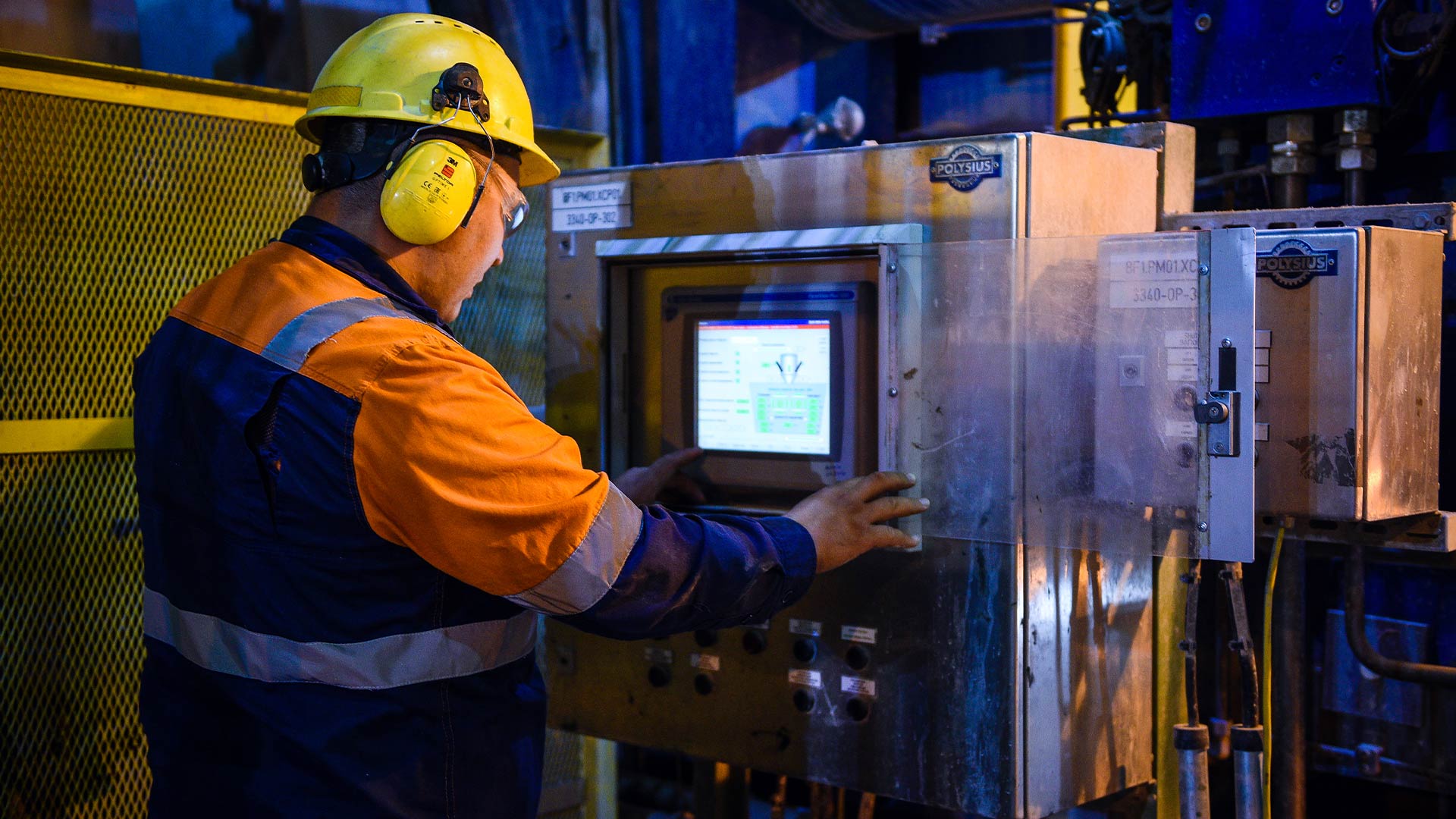 Back view of Kaz Minerals worker wearing protective headgear and clothing looking at a small screen. 